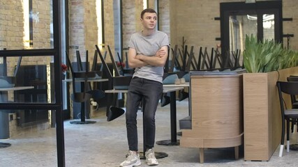Wide shot portrait of sad young restaurant business owner sitting on table in empty cafe during Covid-19 pandemic lockdown, crossing hands and thinking. Bankruptcy crisis. Cinema 4k ProRes HQ.