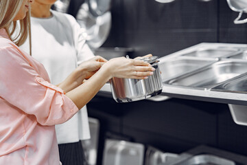 Woman examines various items of dishes. Beautiful woman shopping tableware in supermarket. Manager helps a costumer.