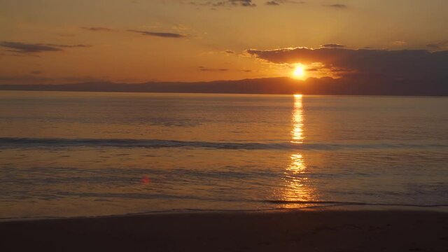 浜辺に寄せる波と西の空に沈む夕日