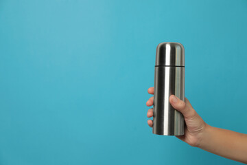 Woman holding modern thermos on light blue background, closeup. Space for text