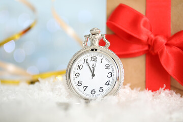 Pocket watch and gift on snow against blurred lights. New Year countdown