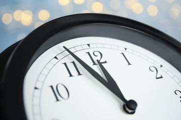 Fototapeta na wymiar Clock on light blue background with blurred lights, closeup. New Year countdown