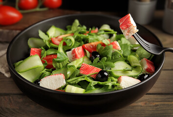 Delicious crab stick salad in bowl on wooden table, closeup