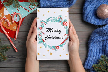 Woman holding Christmas card at grey wooden table, top view