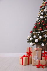 Christmas tree and gift boxes near light grey wall, space for text