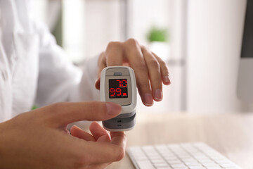 Woman measuring oxygen level with modern fingertip pulse oximeter at workplace, closeup