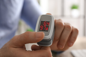 Man measuring oxygen level with modern fingertip pulse oximeter at workplace, closeup