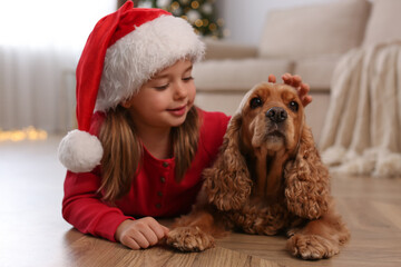Cute little girl in Santa hat with English Cocker Spaniel at home. Christmas celebration