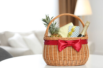Fototapeta na wymiar Wicker basket full of gifts on white table in living room. Space for text