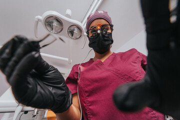 Young blond Caucasian female opening her mouth while African-American ethnic dentist in white latex gloves check condition of her teeth focus on dentist