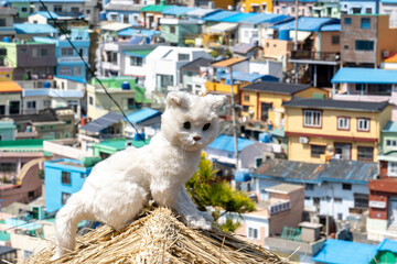 Busan, South Korea - April 6, 2019: A  cat statue on straw roof with Gamcheon Culture Village in background in Busan. The area is known for its steep streets, twisting alleys, and painted houses.