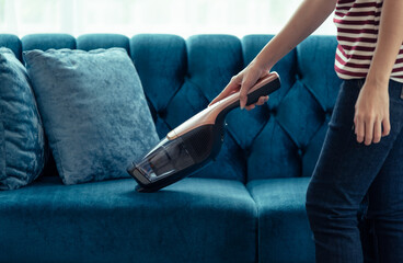 Woman housewife vacuuming furniture in a house with a hand-held portable vacuum cleaner - obrazy, fototapety, plakaty