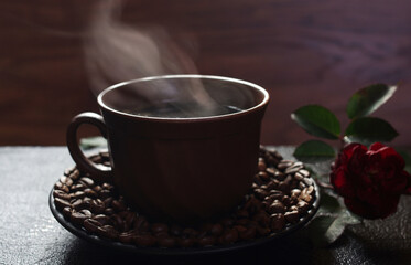 A cup of hot coffee with steam and a red rose. Close-up.