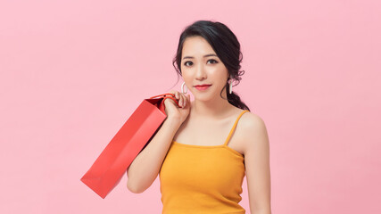 Portrait of pleased girl 20s carrying colorful paper shopping bags while standing isolated over pink background