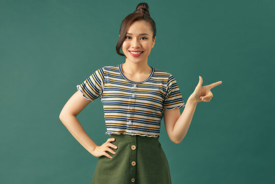 Smiling Asian Woman Stand And Pointing Finger On Green Background.