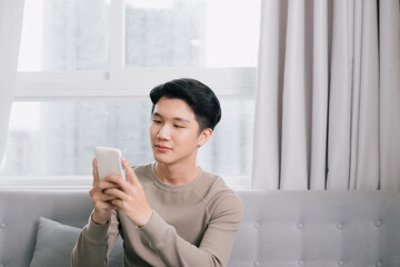 Happy Young Man Relaxing On Sofa And Looking At Cellphone