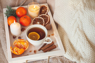 A wooden tray with tea, tangerines, nuts and spices on a beige plaid. Winter breakfast. The concept of hygge.
