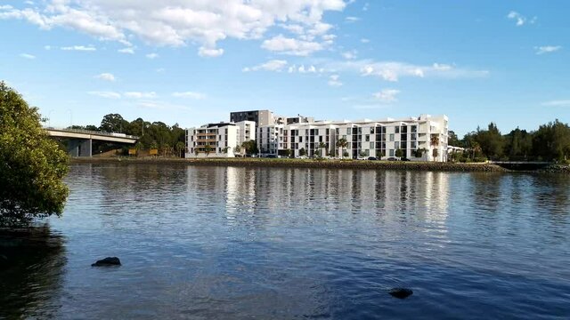 A busy bridge across a calm river with reflections of blue sky, clouds, trees and apartments on water, Parramatta river, Wilson Park, Silverwater, Sydney, New South Wales, Australia

