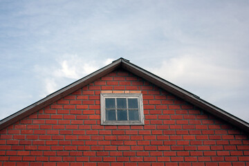 The pediment of a red brick residential building with a window. Fragment of the pediment of the...