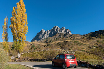 Red car running in small road with yellow poplar tree and mountain peak background in Spain