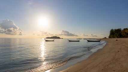 Selective focus of a peaceful beach during sun rise with golden light and blue sky. Fishing boat background