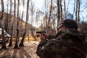 Caucasian man 40 years old with a gas pistol in his hands in camouflage clothes in the forest in...
