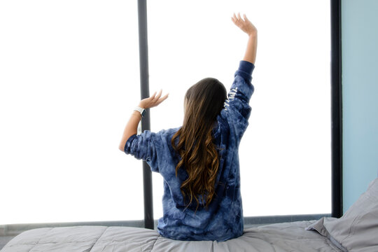 Vista trasera de mujer estirando los brazos en la orilla de la cama viendo hacia la ventana por la ma&ntilde;ana.