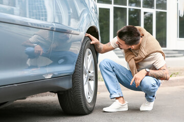 Handsome man checking tires of modern car
