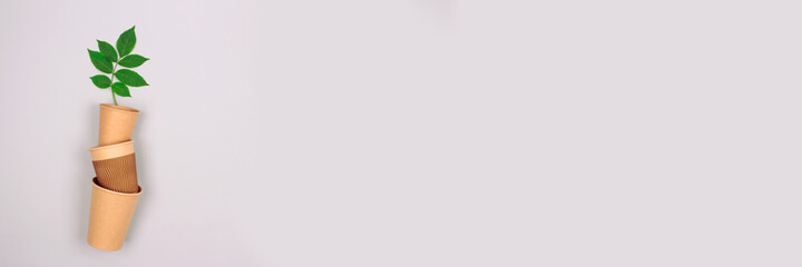 Banner with set of different eco-friendly coffee to go cups - kraft paper cup with green leaves above on light gray background with copyspace. Recycled kraft paper packaging concept, mockup image