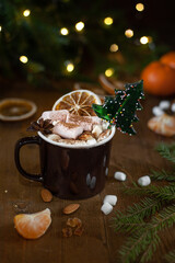 Christmas winter cocoa with marshmallow and lollipop in the shape of a Christmas tree in a brown cup on a wooden background. Vertical photo. Selective focus.