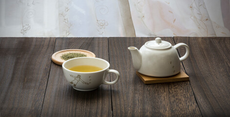 A cup with green tea and Teapot on the wooden table. 