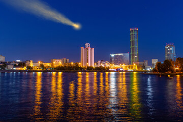 Naklejka premium Comet in the night sky above the city skyscrapers. Reflection in the river