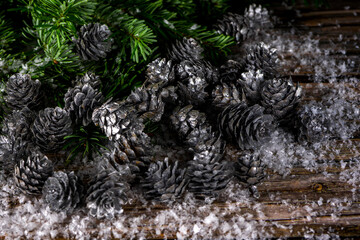 Fir tree branches and silver painted pine cones on a wooden snow background. Christmas symbols. Selective focus