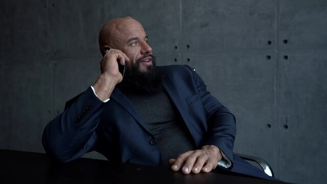 entrepreneur man is communicating by mobile phone sitting in his office, dressed black jacket