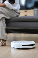 Robotic vacuum cleaner cleaning the living room and woman sitting on sofa at home.