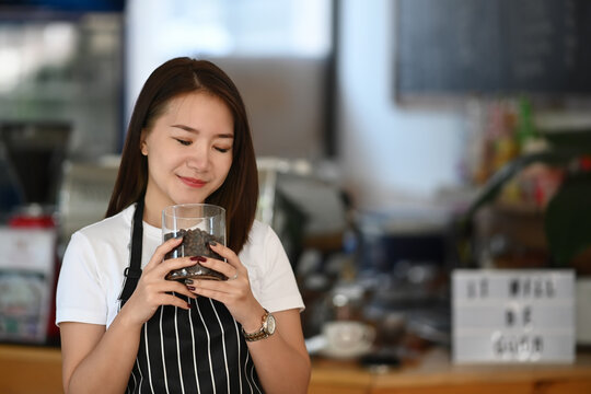 Young woman barista smelling and checking quality of coffee beans at coffee shop. - Powered by Adobe