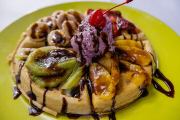 Ice cream, fruit, and chocolate syrup on top of a waffle
