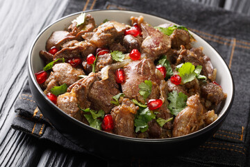 Fried chicken liver, hearts and gizzards with onions, walnuts and pomegranate close-up in a bowl on the table. horizontal