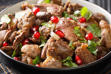 Kuchmachi is a traditional Georgian dish of chicken livers, hearts and gizzards with walnuts and pomegranate seeds close-up in a bowl on the table. Horizontal