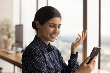 Close up of happy millennial Indian woman look at smartphone screen talk on video call online....