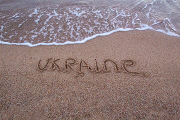The beach with sea waves running on the sand and the  word UKRAINE is drawn on the sand. Beautiful view on the waves