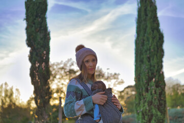 beautiful woman enjoying a sunny afternoon in winter with her baby hanging from a baby carrier. Lifestyle