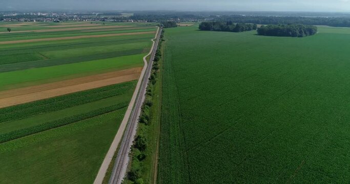 Aerial drone flying over large farming grassland fields. Elevated view of flatland farmland. Agriculture agronomy concept. Straight railway railroad between fields. Backward moving