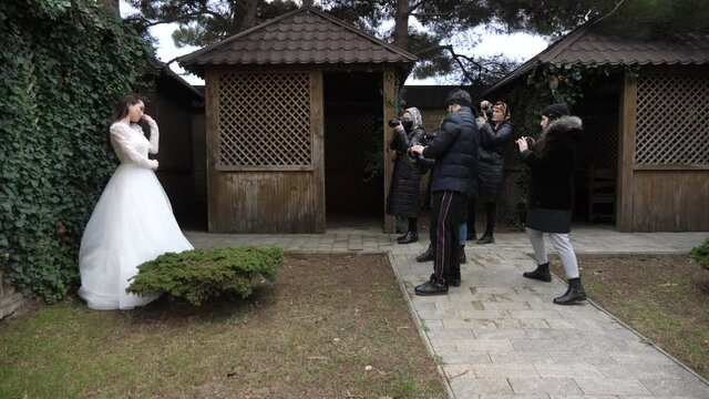 Group of professional photographers takes pictures of elegant bride wearing gorgeous white wedding dress in restaurant yard