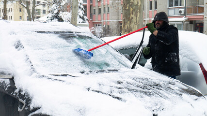 Man clears snow from icy windshield of car.