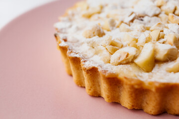 Delicious apple tartlet with caramelized apple, custard cream, roasted nuts and powdered sugar served on a pink plate with light background. Selective focus. Copy space.