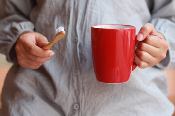 Woman hands holding wooden bamboo toothbrush with red mug , sustainable lifestyle, zero waste...