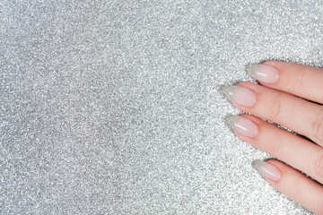 Closeup top view flatlay photography of female fingers with beautiful elegant pastel french nail design of pink and silver colors isolated on sparkling silver background with copyspace. Holiday nails.