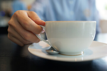 Coffee to go. Close up female hand holding a cup of hot latte on a wooden table in a cafe.