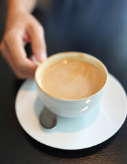 Coffee to go. Close up female hand holding a cup of hot latte on a wooden table in a cafe.